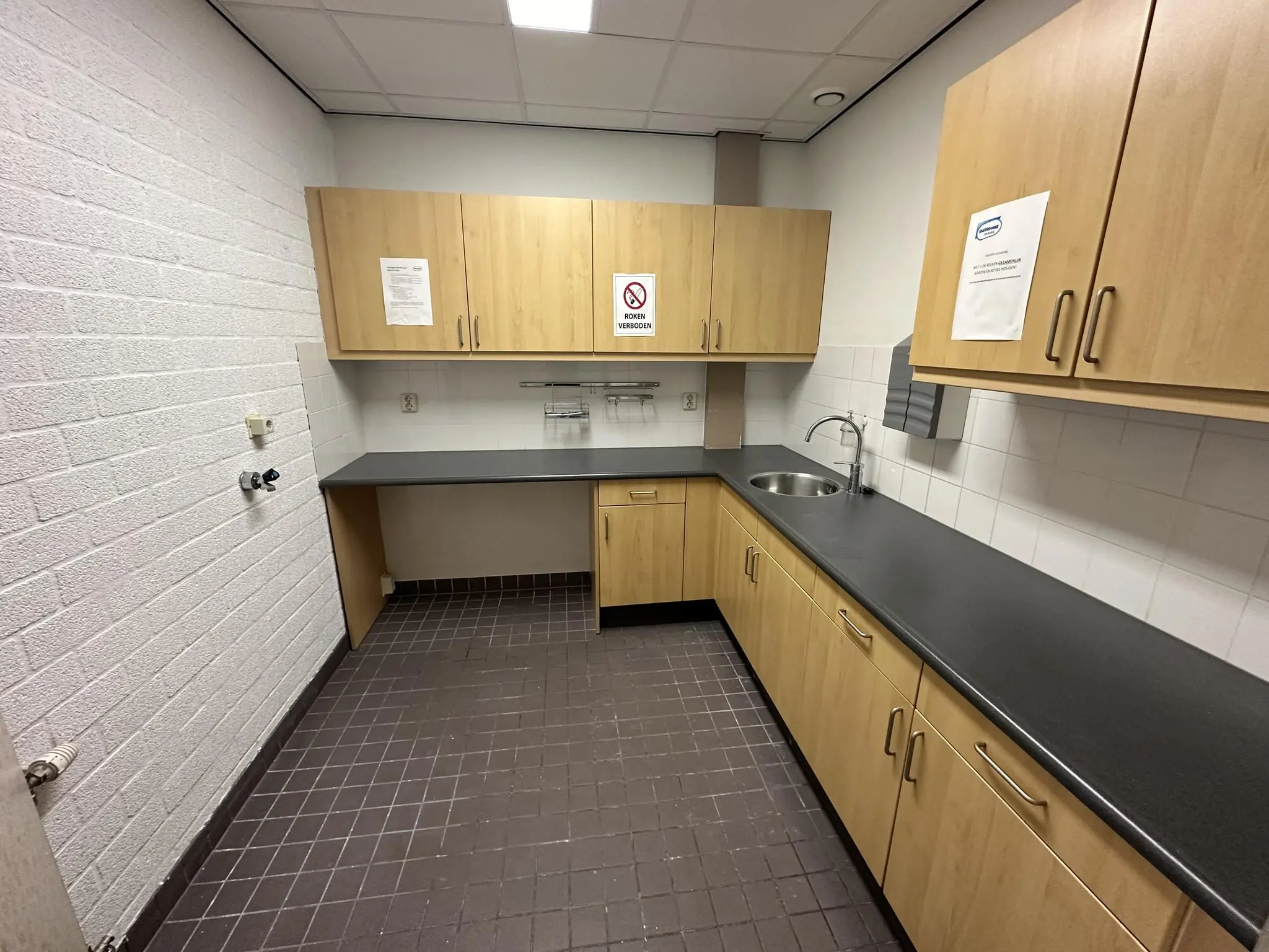 Kleine bedrijfskeuken aan de Van der Hagenstraat met houten keukenkastjes, grijs werkblad en witte tegelmuur.